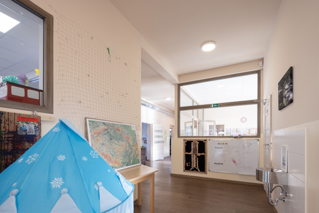 Společná chodba školy s mapou, plakáty a modrým hracím teepee
