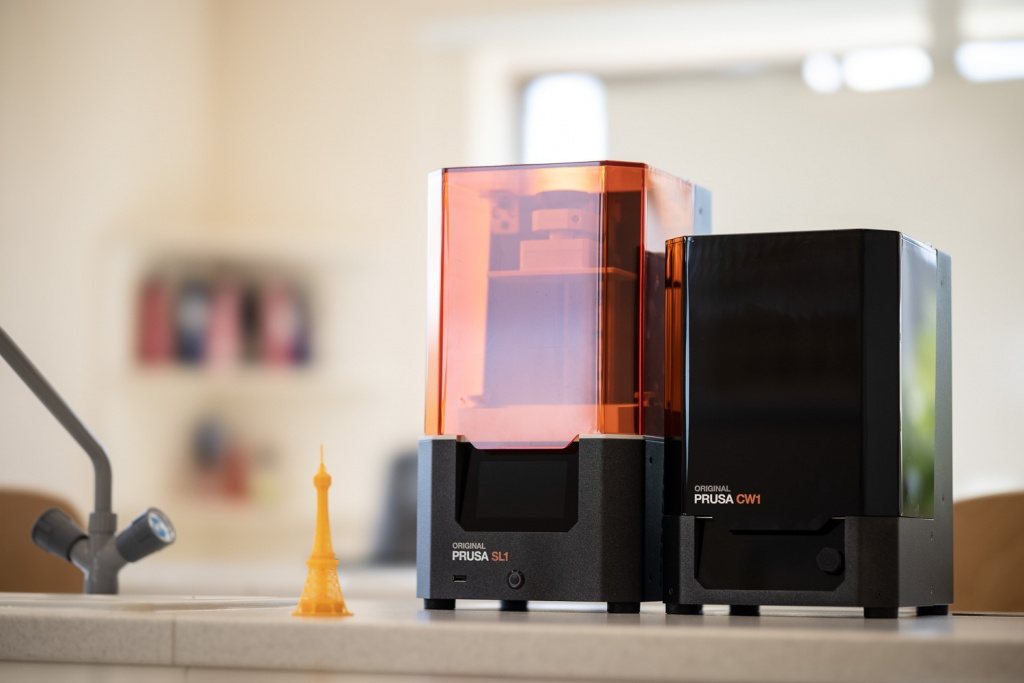 Dvě 3D tiskárny, jedna s oranžovým krytem